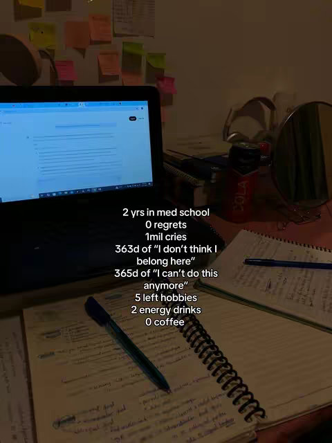 A dimly lit desk with a laptop open, notebooks, and papers scattered around. A can of cola sits on the desk, along with a pen, and a small mirror. Text overlays in white font list humorous statistics about the struggles of medical school.