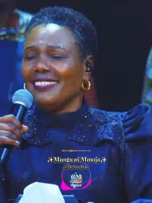 The cover image features a woman with short, dark hair, wearing a dark-colored dress. She holds a microphone, facing slightly to the left, with a soft smile. The background appears to be a stage, dimly lit, possibly during a performance. Text overlays, including the phrase "Mungu ni Mmoja," and a logo are present in the image.