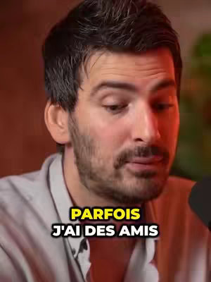 A medium shot of a man with dark hair and a beard, set against a vaguely orange background with a microphone to the side. Text overlays appear in a yellow box towards the middle-bottom of the image.