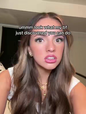 A selfie-style video cover image featuring a young woman with long, highlighted hair and expressive makeup. She has a slightly open mouth as if in surprise or initial reaction. The background appears to be a simple indoor setting.