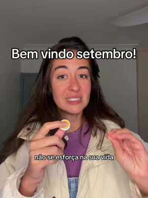 A woman with long brown hair is facing the camera, holding a small, circular object, likely a token or charm. The background is a home interior, with neutral-colored walls and ceiling. The woman appears to be speaking, and the image includes text overlays.