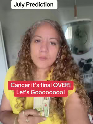 A woman with curly brown hair is centered in the frame, wearing a yellow shirt. Above her head, a white rectangular box reads "July Prediction". A red rectangle at the bottom is used as a hook that says "Cancer it's final OVER!
Let's Goooooooo!". The background is a slightly blurry interior space with plants, a sink, and a pendant light providing a minimalistic setting for the content. The woman is holding a tarot card.