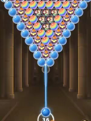 The cover image shows a screenshot from a bubble shooter game. At the top, there is a triangle of colorful bubbles. Below them are rows of blue bubbles with patterned designs. In the firing position, a single blue bubble is connected by a blue line to a white circle at the bottom with the number '36'. The background is a blurred perspective of a hallway with pillars, with a general color scheme of golds and blues.