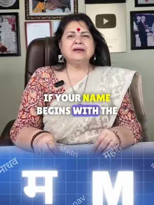 The cover image features a woman centered, seated, and facing the camera. She wears a patterned red and brown blouse with a cream shawl draped over it. Her face is framed with dark hair and a bindi. The background shows framed pictures and a YouTube play button award. Overlaid on the lower part of the image is text informing viewers about the video's subject. Two logos with the letter 'M' are at the bottom