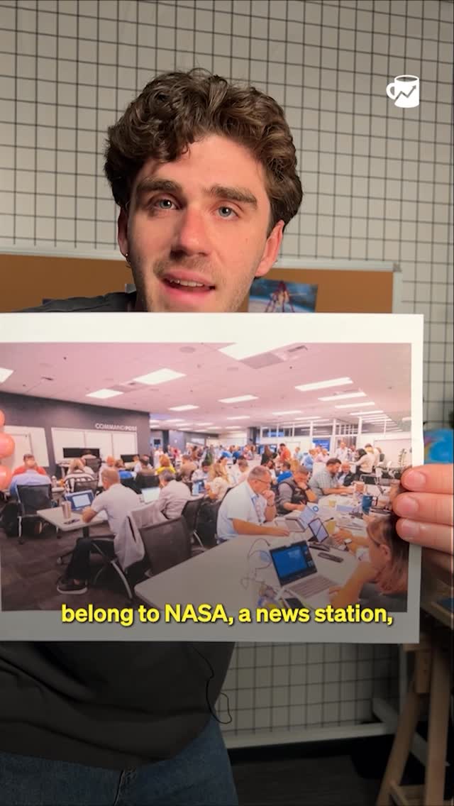 A man is holding a printed image of a busy office setting, potentially a newsroom or control center. The background features a grid pattern and a whiteboard, suggesting an interior location. Text overlayed on the presented image states "belong to NASA, a news station".