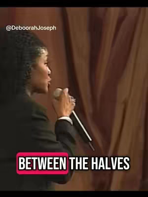 A woman, seen in profile, is holding a microphone and speaking, set against a stage or background with draped fabric. The image has a warm color palette dominated by browns and tans. Added text overlay reads 'BETWEEN THE HALVES'.