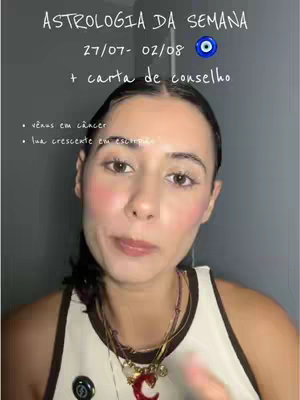 A selfie-style image featuring a woman looking at the camera with a slight smile. She is wearing a white tank top with brown trim and several necklaces. Text overlays state "ASTROLOGIA DA SEMANA 27/07- 02/08 + carta de conselho", alongside bullet points "vênus em câncer" and "lua crescente em escorpião". The background is a plain, dark surface.