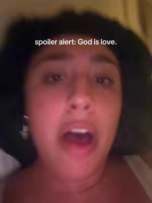 A close-up shot of a woman with dark hair, her face filling the frame. She has a slightly open mouth, suggesting speech or surprise. The background is blurred, indicating an interior setting. The text 'spoiler alert: God is love.' is overlaid at the top.