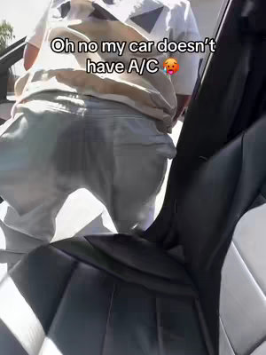 The image shows a person getting out of a car. The person is wearing light-colored pants and a white shirt with a geometric pattern. The car interior is black. Text overlay shows the phrase "Oh no my car doesn't have A/C"