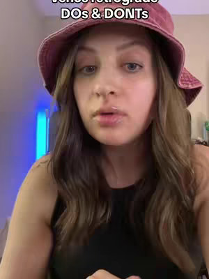 A woman with long brown hair wearing a pink bucket hat is centered in the frame, looking towards the camera. The background is slightly blurred, suggesting an indoor setting, and a blue light is visible behind her.