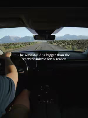 The image shows a view from inside a car, looking out through the windshield onto a road stretching towards mountains. Text is overlaid on the image.