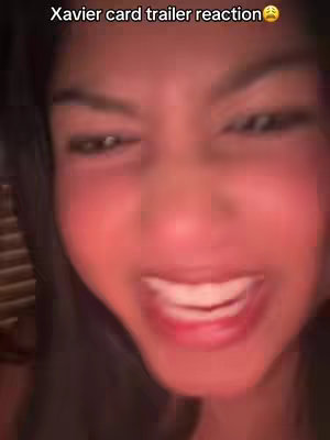 A close-up shot captures a young woman's face, likely in a selfie. Her expression is animated, with a wide smile and shining eyes, suggesting excitement or amusement. The lighting seems warm and natural, focusing on her face and the details of her features. The background is out of focus, keeping all attention on her reaction.