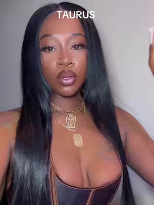 A woman with long, black hair is centered in the frame against a plain background. She has dark skin, full lips, and is wearing multiple gold necklaces. A text overlay at the top of the frame reads 'TAURUS'.