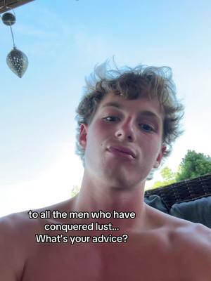 A young man with short, tousled hair faces the camera from a low angle, with a partly visible background of a light blue sky and foliage. A circular object hangs at the top left corner, presumably decor. Text overlays the lower section of the frame.