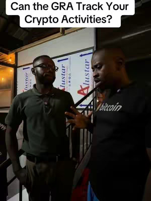 Two men are in a conversation in front of a background of partially visible informational boards. The man on the right is speaking while gesturing. The other man on the left is listening. The scene has a mix of artificial and natural lighting.