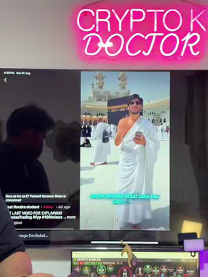 A man in white robes stands in front of the Kaaba in Mecca, holding a phone. The background shows a large crowd. On the top a pink neon sign reads CRYTPO DOCTOR.