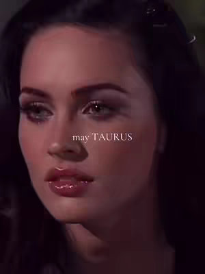A close-up shot of a woman's face, soft lighting, with the words 'may TAURUS' overlaid. The background is dark, focusing attention on the subject's face, with slightly blurred details. The color palette leans towards warm tones.