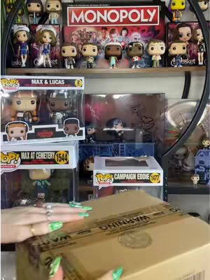 The cover image shows a collection of Stranger Things Funko Pop figures on shelves, including various characters like Max, Lucas, and Eddie Munson, with a Monopoly board game box. In the foreground, the hands of a person with painted nails are opening a cardboard box. The overall composition is cluttered but organized, with a focus on the collectibles.
