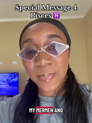A head-and-shoulders shot of a Black woman with long, dark hair pulled back into a low ponytail. She is wearing diamond-shaped, light-tinted glasses. The woman has a slight smile and is looking slightly to her right. The background appears to be a wall and possibly, a small part of furniture.