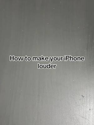 A plain, grey surface background with the text 'How to make your iPhone louder' in a black font, centered on the image.
