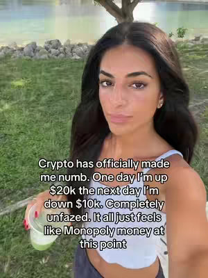 A selfie-style video cover image of a woman in a white top, holding a drink, with a waterfront background and overlaid text. The woman has long dark hair and appears to be outdoors on a sunny day. Behind her, a body of water and greenery are visible.