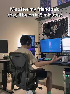 A man with headphones is sitting in a gaming setup in front of a computer monitor, looking to the side with an exasperated expression. The room is in a neutral color palette, with the lighting of the screen reflecting on his face.