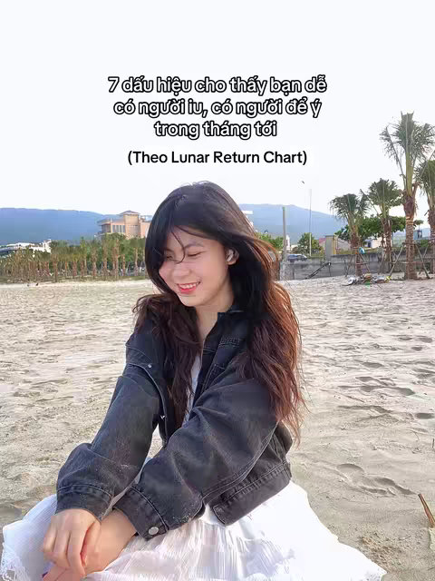 A young woman is sitting on a sandy beach smiling. She has long dark hair and is wearing a black denim jacket over a white top and skirt. Text overlays above the woman provides context and prompts the viewer.