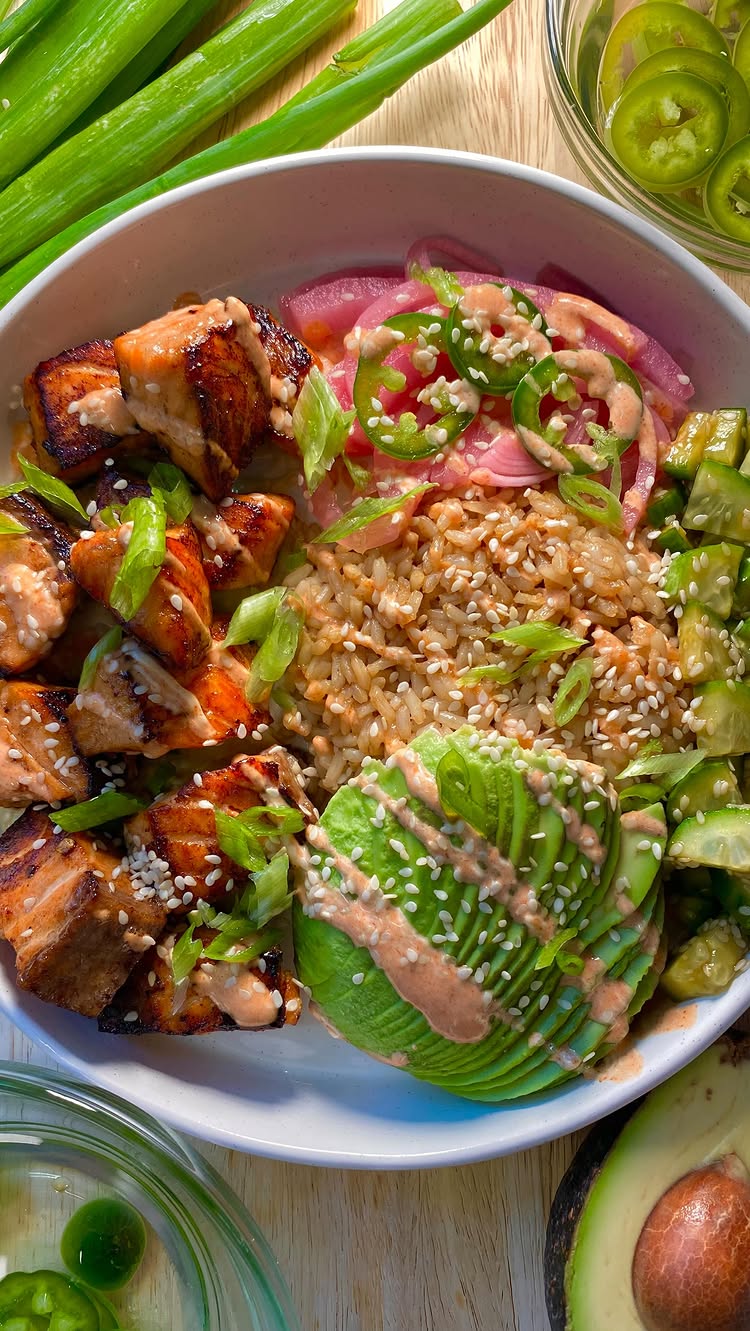 An overhead shot of a vibrant salmon bowl, with sections for salmon, rice, avocado, onions, and jalapeños. The bowl is set on a wooden surface, and green onions and jalapeños are arranged around it. The colors are natural, with the salmon and avocado as the focal points, and the layout appears appetizing and well-composed.