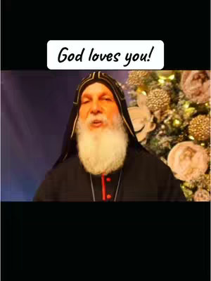 The cover image features a man with a white beard, wearing a black robe with a hood and a red accent under his neck. The background is somewhat blurred with floral decorations and the image has a black border. A white box with the text "God loves you!" is over the image.
