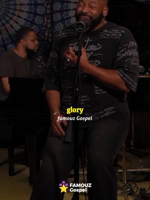 The image shows a man singing into a microphone with the text "glory famouz Gospel" overlaid on top. He is wearing a black top and is positioned in front of a piano.