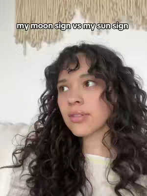 A young woman with curly dark hair is looking off to the side with a thoughtful expression. The text overlay reads "my moon sign vs my sun sign."