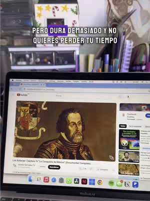A laptop displaying a YouTube video is the central focus, with a historical painting visible on the screen. Text overlays are present. The background is blurred but suggests a cluttered desk area. The overall composition seems informal, focusing on the content displayed on the laptop.