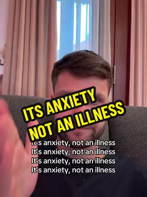 A selfie-style video cover features a man centered in the frame, with text overlays that read 'ITS ANXIETY NOT AN ILLNESS' in a large, bright yellow font with black trim. Below this repeated text is a statement, 'It's anxiety, not an illness' multiple times in a smaller font. The man has short brown hair and appears to be indoors, with a blurred background that includes curtains and likely a window. His right arm is slightly visible, and his skin tone appears fair, with a neutral emotional expression.