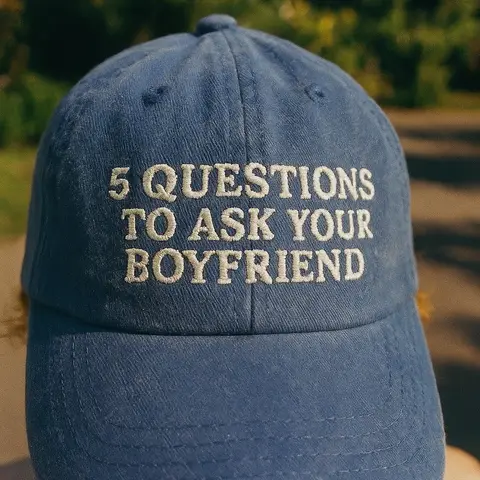 The cover image shows a close-up of a blue denim baseball cap. The cap has white embroidered text that reads "5 QUESTIONS TO ASK YOUR BOYFRIEND". The background is blurred, suggesting an outdoor setting.