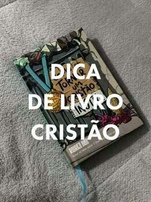 The image features a book atop a textured gray surface. The book has a colorful cover with text overlaid in white, advertising a book recommendation for christians. The composition is a close-up shot with soft lighting.