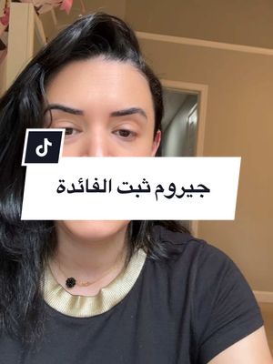 A selfie-style video cover featuring a woman with dark hair looking down at the camera. She is wearing a black top and a necklace. A white rectangular box overlay contains Arabic text. The background shows a room with beige walls and a doorway.
