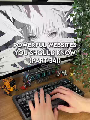 A desktop setup with a computer monitor displaying a black and white anime-style illustration. In front of the monitor is a keyboard with the creator's hands typing. There are decorative items on the desk, including a clock-like device and miniature figures, with background foliage adding a touch of life.