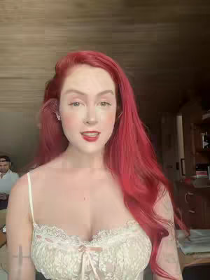 The cover image features a woman with bright red hair, red lipstick, and light makeup. She is wearing a cream-colored top with lace detailing. A man is partially visible in the background. The composition is a close-up shot, focusing on her upper body and face.