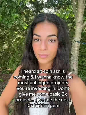 A selfie-style video cover image featuring a young woman with long, dark hair. She is looking directly at the camera. Overlaid on her image is a text asking viewers to provide their cryptocurrency investment recommendations. The background is slightly blurred, revealing green foliage and hints of a tree.