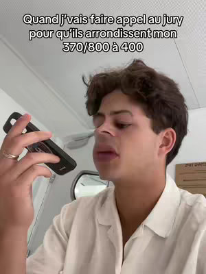 A young man with dark hair and a white shirt holds a black phone to his face, talking with a slightly emotional expression. Text overlays are present at the top of the image.