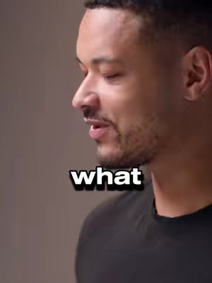 A medium shot featuring a man in a black t-shirt. He is positioned slightly off-center, with his head turned towards the left, mid-speech. Below him, against a neutral background, the word 'what' is superimposed in a bold, white font with a black outline.