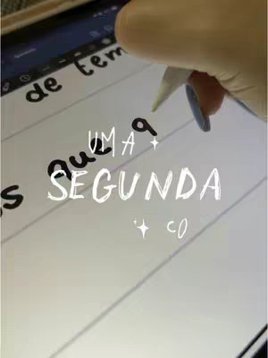 The image shows an iPad with text written on it. The text says "Uma segunda co", with the word segunda in a distinctively stylized font. A hand holding a stylus is visible, presumably writing on the iPad screen. The background is a lightly visible notes.