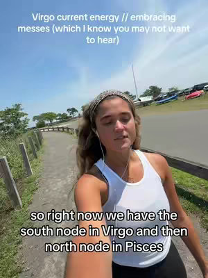 A woman is walking on a path with her phone. Overlay text at the top says 'Virgo current energy // embracing messes (which I know you may not want to hear)' and text at the bottom that says: 'so right now we have the south node in Virgo and then north node in Pisces'.