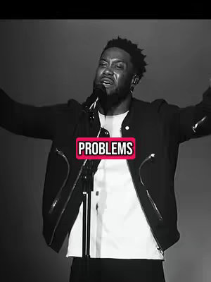 A grayscale image featuring a Black man with a microphone, arms raised. The word "PROBLEMS" is overlaid in a pink rectangular box. Behind him is a dimly lit, dark background.