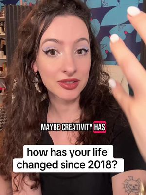 A woman with long curly hair and makeup is centered in the frame, facing the camera and speaking. She has a tattoo on her left arm. The background subtly features a patterned wall and a glimpse of a bookshelf. Text overlays are present at the bottom and on a colored box in the middle of the image.