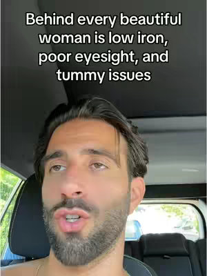 A man sits in the driver's seat of a car, looking towards the camera against a background of a sunny day through a clear windshield. The caption reads: 'Behind every beautiful woman is low iron, poor eyesight, and tummy issues'.