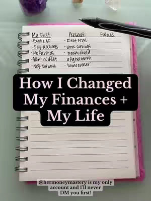 An open notebook is laid on a light-green surface, featuring handwritten lists and a large text overlay. The title text in a black rectangular overlay reads, "How I Changed My Finances + My Life," standing out against a background of lined paper. In the top left corner, a purple crystal is seen, and to the right, a pen rests on the notebook with the tip pointing towards the right side. The notebook is pink near the spine and has silver rings.