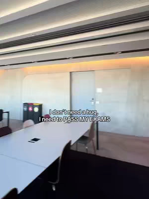 Interior shot captures a well-lit modern room, possibly a study or office, dominated by a large white table. The table stretches into the distance with chairs arranged around it. In the background, a closed door and a trash receptacle are visible. The lighting is warm, highlighting the clean lines and minimalist design.