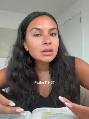 A woman with long dark hair is centered in the frame, looking towards the viewer with a slightly inquisitive expression. She is in front of an open book resting on a table. The overlay text reads 'Psalm 119:37'.
