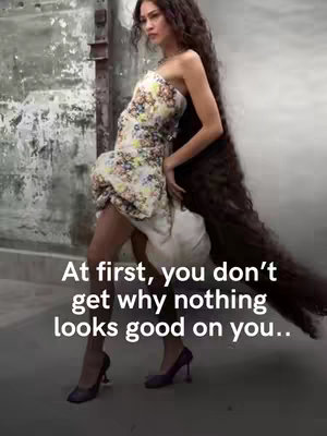 A woman with long, dark hair poses in a floral patterned dress and high heels against a blurred background. The text overlay reads "At first, you don't get why nothing looks good on you.."